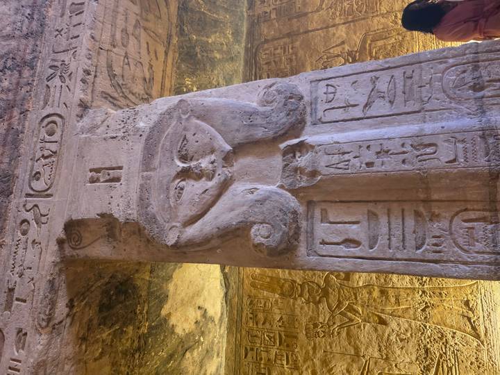 Column capital carved with face of Hathor and hieroglyphs in Egyptian temple interior.