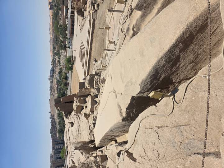 Site of the unfinished obelisk quarry with large cracked stone block and cityscape in background.