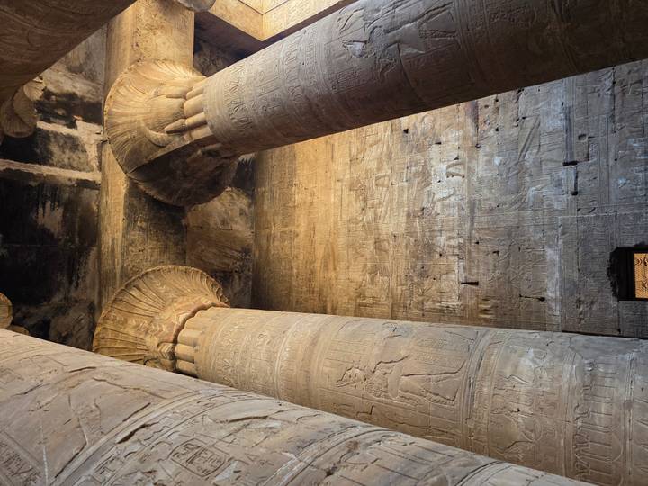 Interior hall with massive decorated columns and weathered sandstone walls of an Egyptian temple.