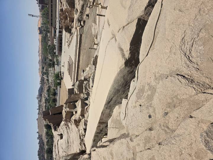 Another angle of unfinished obelisk quarry with sandy floor and distant buildings.