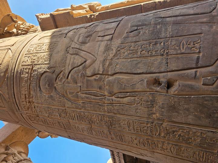 Carved relief of goddess on sandstone column with deep shadows inside Kom Ombo temple.