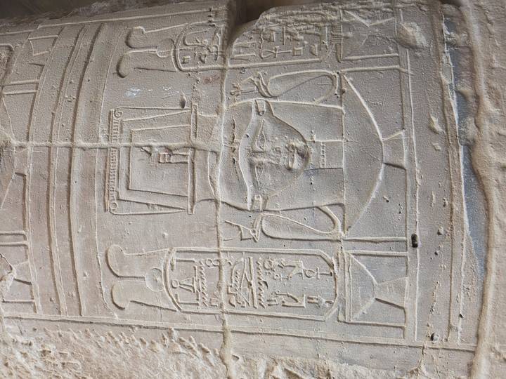 Weathered carving of Hathor-like face and cartouches on temple column surface.