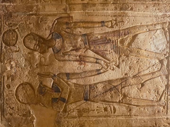 Golden-lit relief showing two ancient Egyptian figures clasping hands.