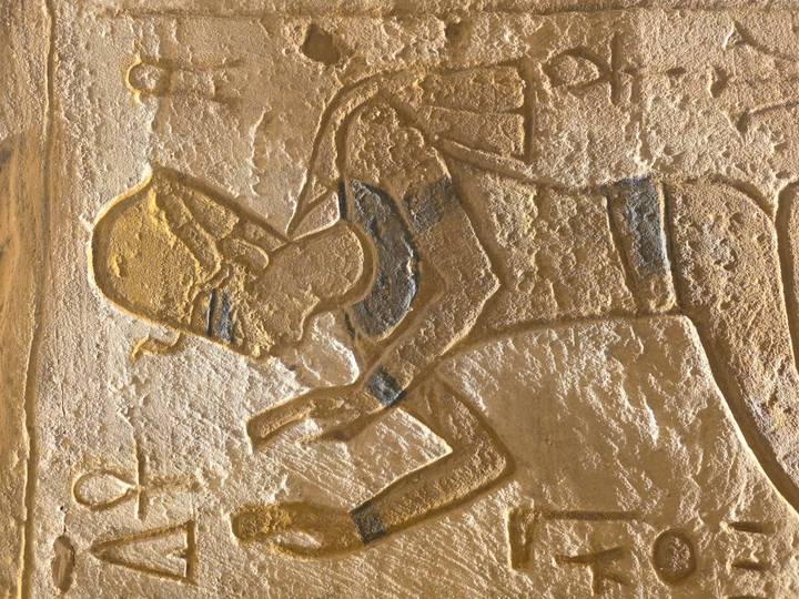 Close-up relief of pharaoh offering gesture, highlighted by sunlight.