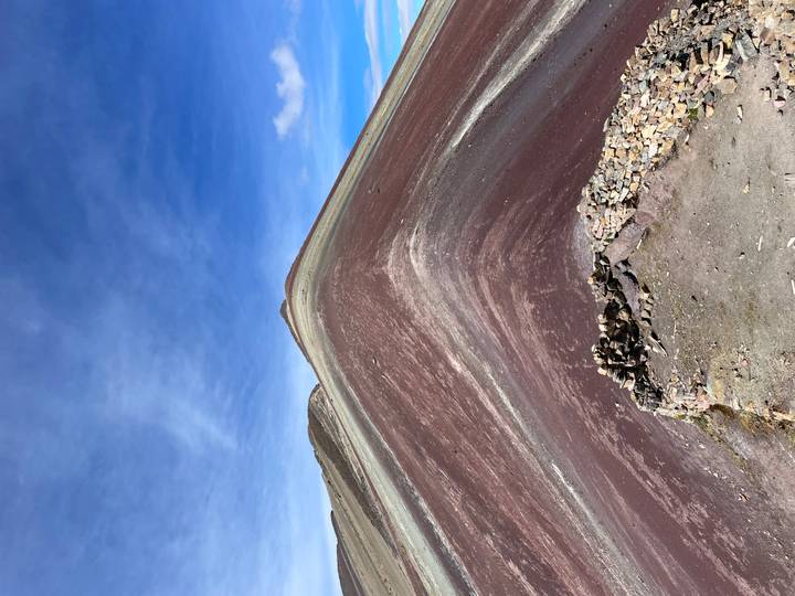 Sharp ridge of Rainbow Mountain displaying maroon and cream mineral layers against blue sky