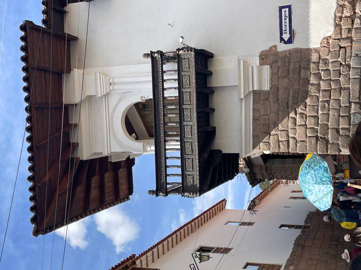 Ornate carved wooden balcony projecting from a white colonial façade in Cusco