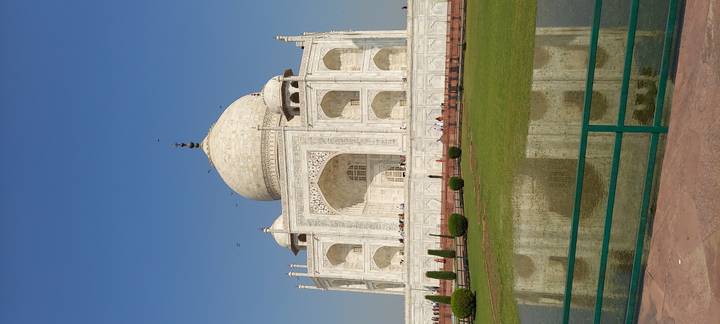 Full side view of the Taj Mahal reflected in foreground pool under clear blue sky