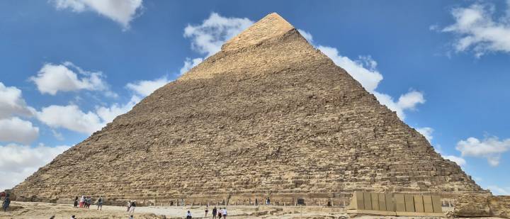 The Great Pyramid of Giza towering over visitors under a blue sky with clouds