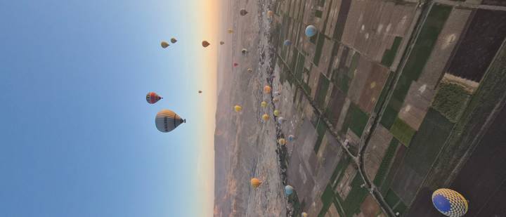 Dozens of hot-air balloons floating over patchwork farmland at sunrise in Luxor