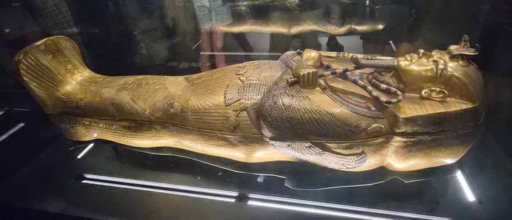 Golden sarcophagus displayed in a museum exhibit under dim lighting