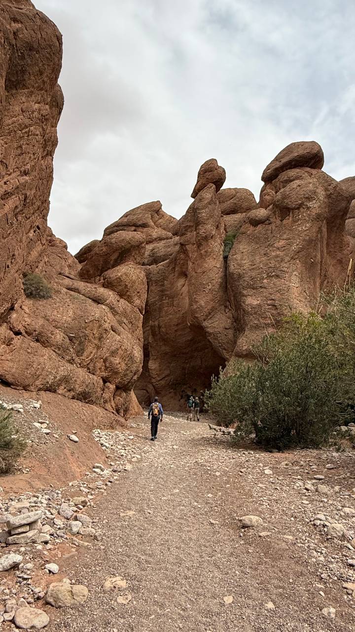 Hikers dwarfed by towering red sandstone cliffs in narrow gorge.