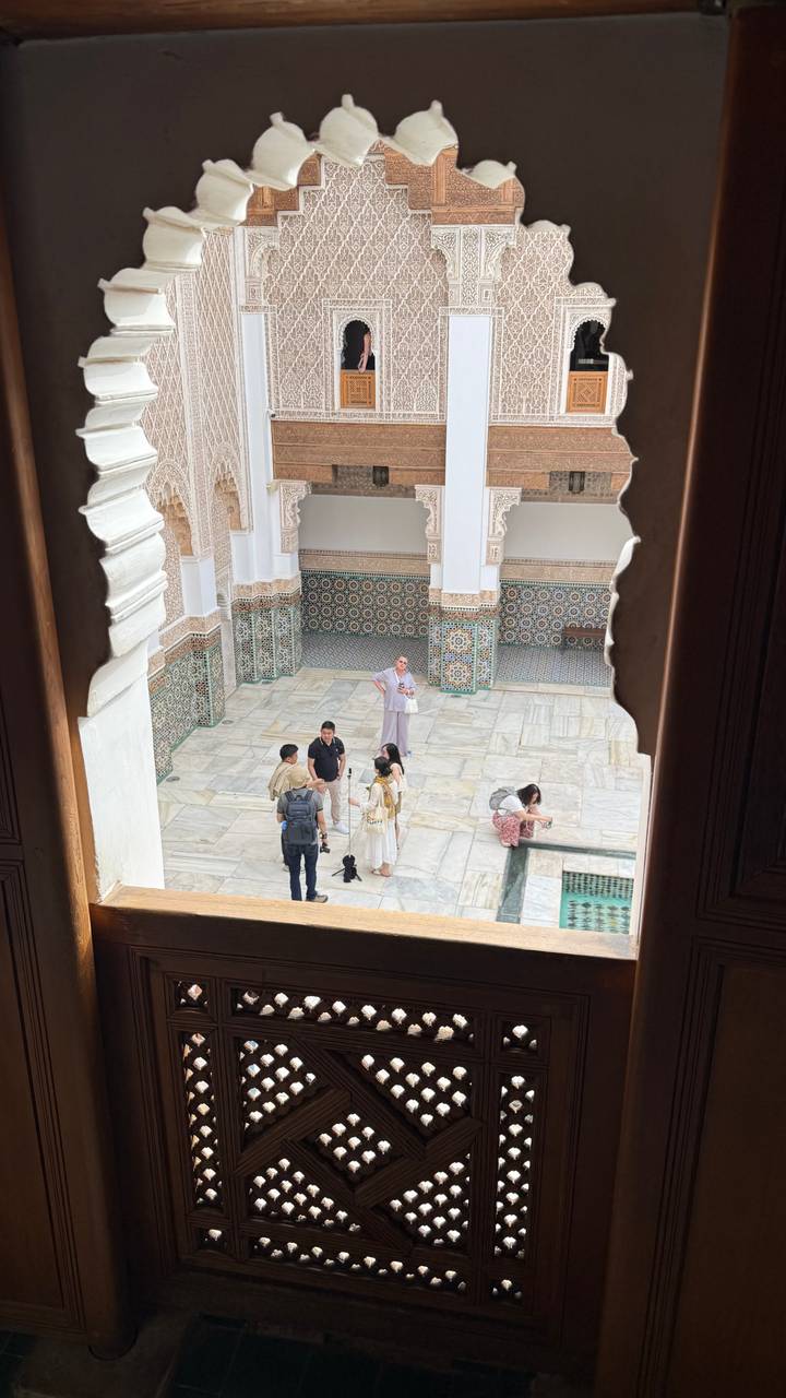 Visitors conversing in ornate courtyard with patterned tile walls viewed through decorative arch.