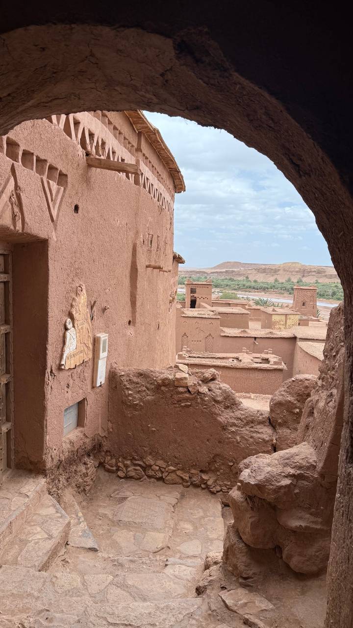 View over the earthen kasbah buildings of Ait Benhaddou with a river and arid hills in the background.
