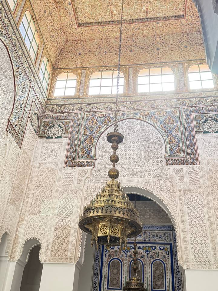 Ornate interior of a Moroccan mosque or madrasa with detailed stucco and colorful tilework.
