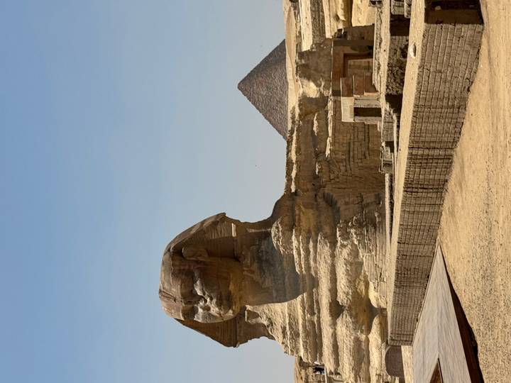 The Great Sphinx of Giza with a pyramid rising behind under a clear desert sky.