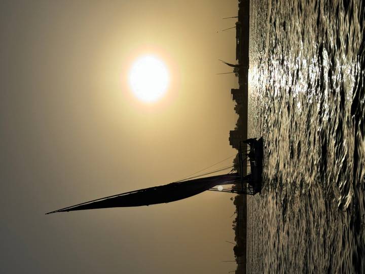 Traditional felucca sailboat glides on the Nile at sunset with shimmering water and orange sky.