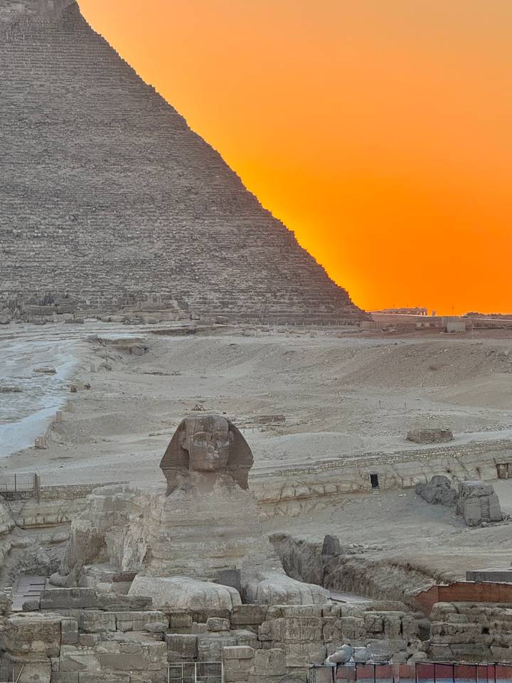 The Sphinx in the foreground with pyramid silhouettes against a vivid orange sunset sky.