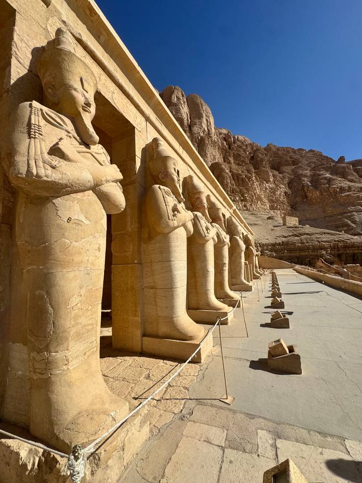 Row of colossal Osiride statues line the terrace of Hatshepsut’s temple against desert cliffs.