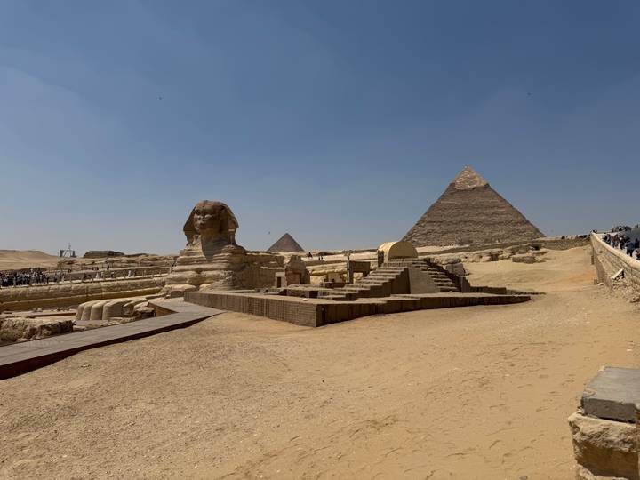 The Great Sphinx facing the Pyramid of Khafre under a clear blue sky with a wooden walkway leading through the sand