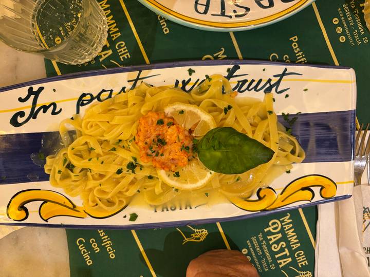 Plate of tagliatelle pasta topped with creamy salmon sauce, basil leaf and lemon slice on decorative ceramic dish