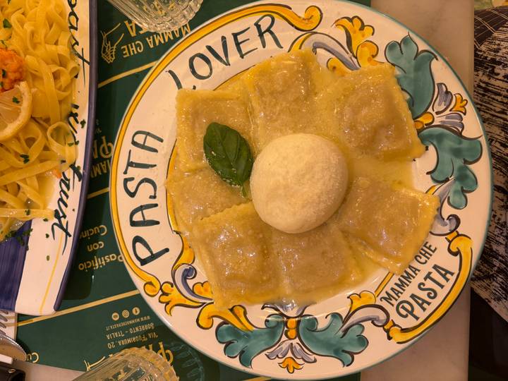 Ravioli arranged around a ball of mozzarella in buttery sauce on a colourful 'Pasta' plate