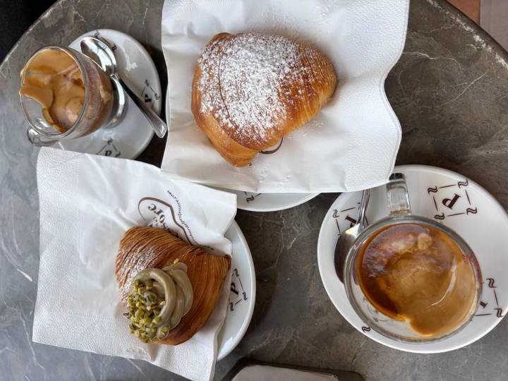 Close table shot of croissants, pistachio sfogliatella and tiny cups of espresso on marble surface