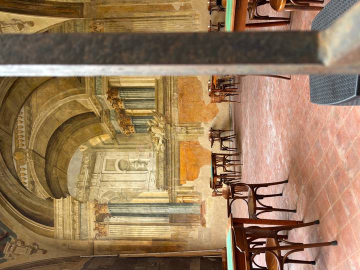 Atmospheric cafe courtyard with empty wooden tables set against grand frescoed Renaissance arches