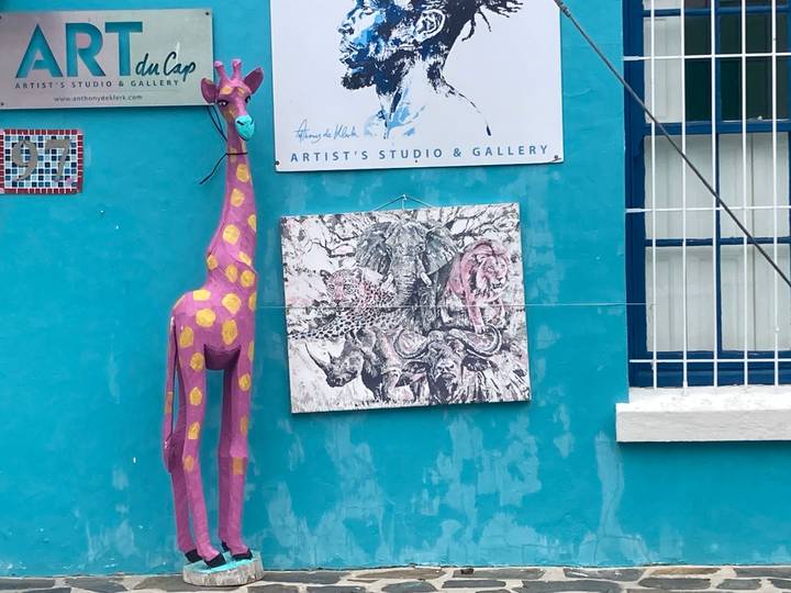 Colorful turquoise wall with modern African art, a pink spotted giraffe sculpture and a gallery sign in Bo-Kaap