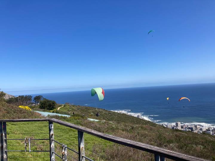 Several colorful paragliders soaring above Signal Hill with Cape Town and the Atlantic Ocean below