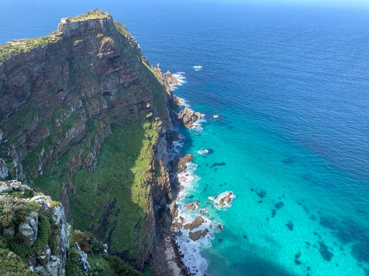 Dramatic cliff dropping to bright turquoise waters at Cape Point on a sunny day