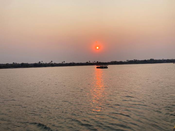 Fiery red sun setting over a wide river with a small cruise boat reflecting on the water