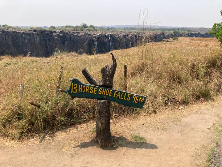 Wooden trail sign reading 'Horse Shoe Falls 45m' with Victoria Falls gorge in the background