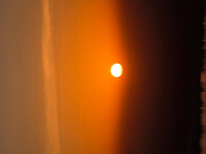 Brilliant orange sun setting over a hazy horizon.