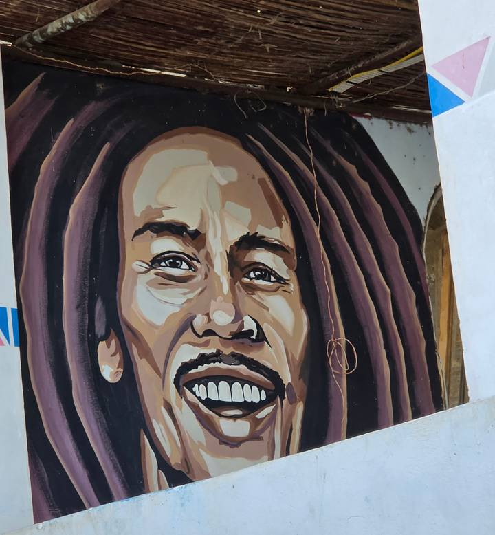 Close-up of a vibrant mural depicting a smiling face with dreadlocks on a Nubian house wall.