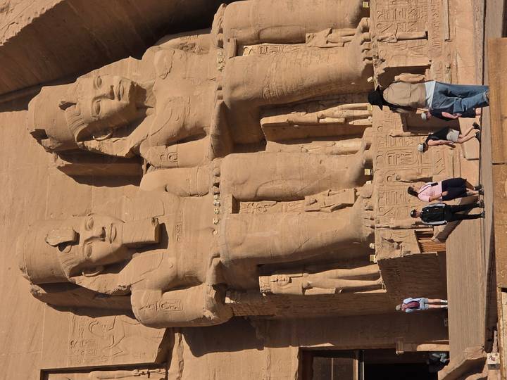 Massive seated pharaoh statues of Abu Simbel basking in bright sunlight as tourists gather below.