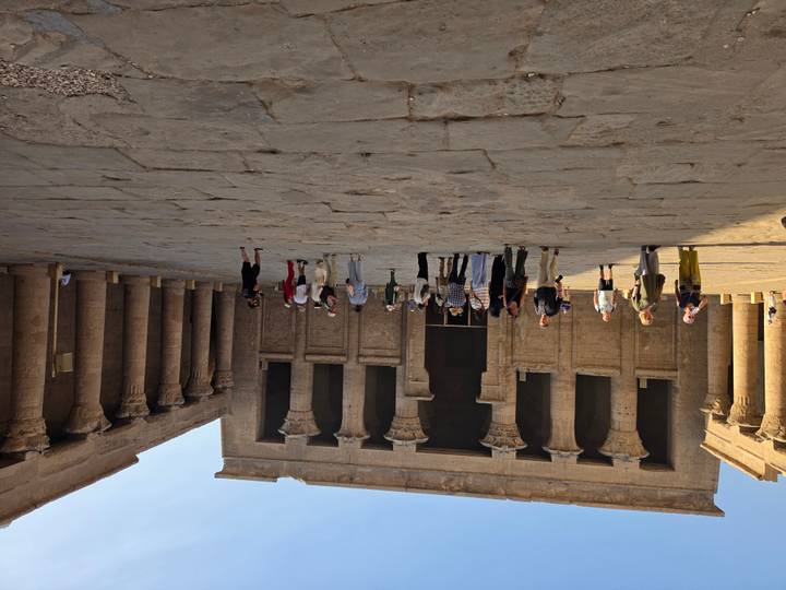Wide courtyard inside an ancient temple with groups of tourists surrounded by towering columns.