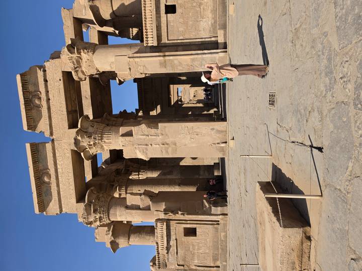 Entrance columns of Kom Ombo Temple with tourists, captured under bright sun.