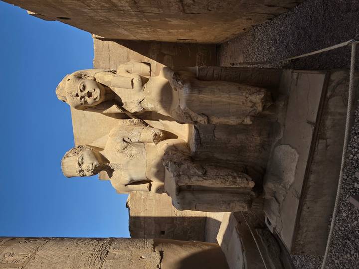 Pair of weathered seated pharaoh statues missing limbs inside an ancient temple.