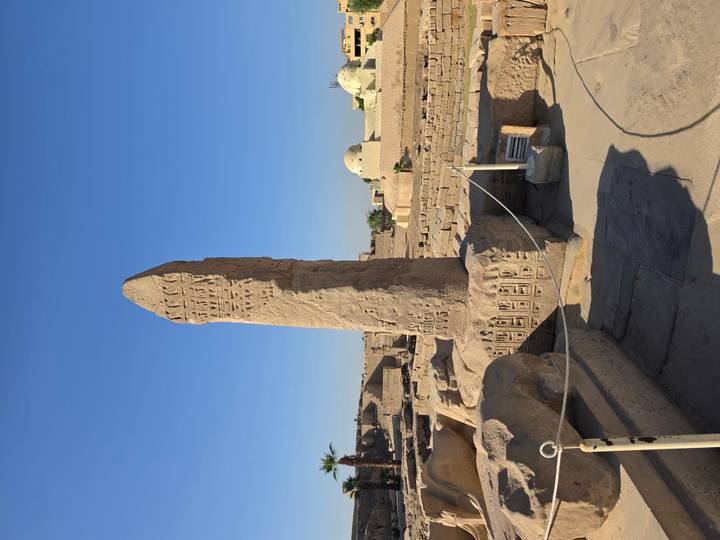Tall sandstone obelisk covered in hieroglyphics within the ruins of an ancient Egyptian temple complex.
