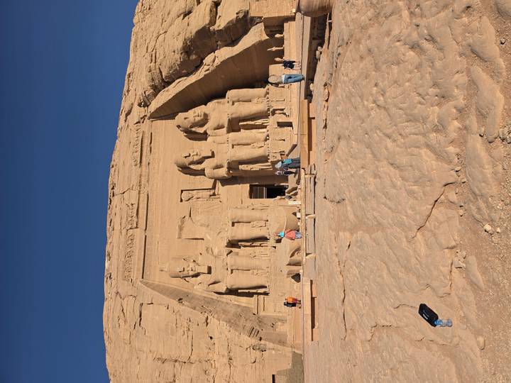 Grand facade of Abu Simbel temple with four colossal seated statues and tourists at the entrance.