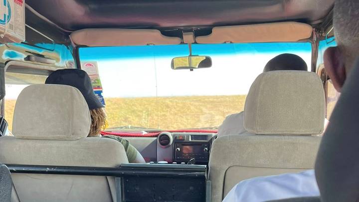 View from the rear seat inside a safari jeep looking through the windscreen toward open savannah.