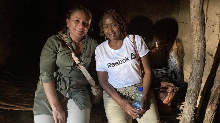 Two women seated inside a dimly lit traditional mud hut, smiling for the camera.