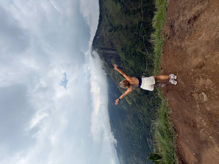 Woman with open arms looks over misty green mountains and valleys under dramatic clouds