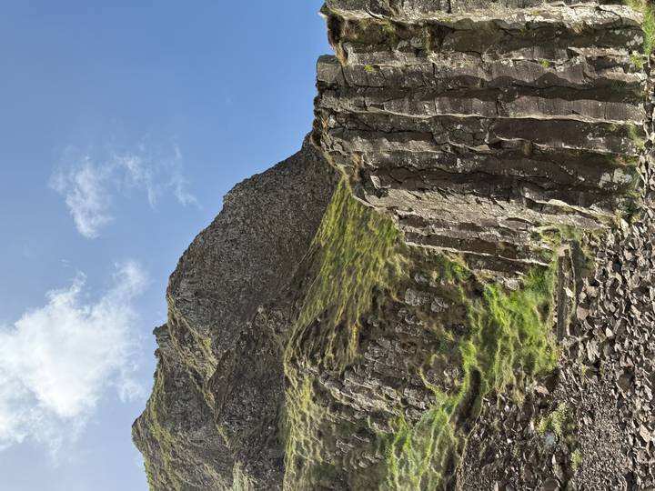 Basalt columns rising from a grassy slope beneath a rugged mountain ridge