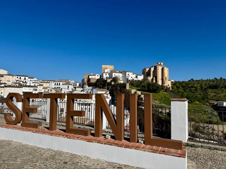 Large metal letters spelling SETENIL with white hill town and castle in the background