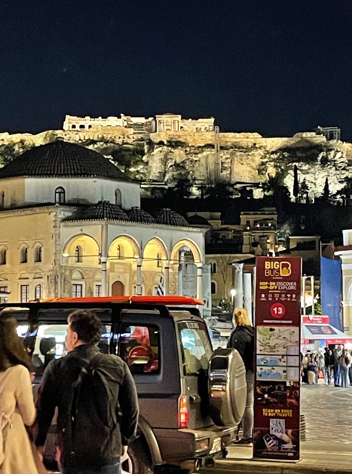 Nighttime street scene in Athens with lit mosque-like Tzistarakis Mosque and tour bus stop sign