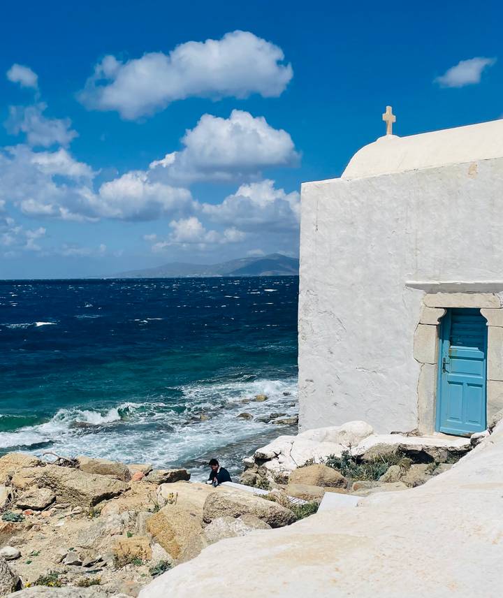 Bright blue Aegean Sea crashing against rocks beside a whitewashed wall and turquoise door