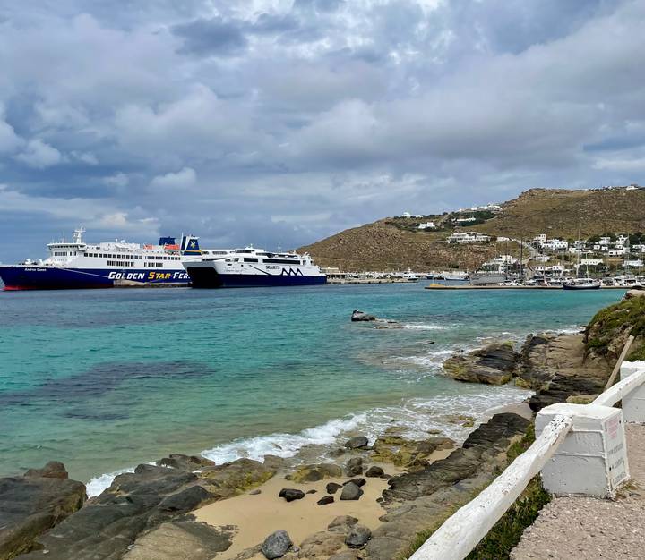Two large ferries anchored in turquoise harbor waters with hillside village beyond