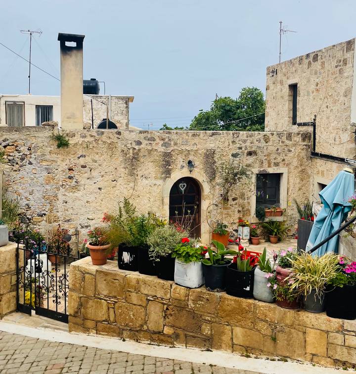 Charming stone courtyard with arched wooden door, climbing vines and potted flowers on a Greek island.