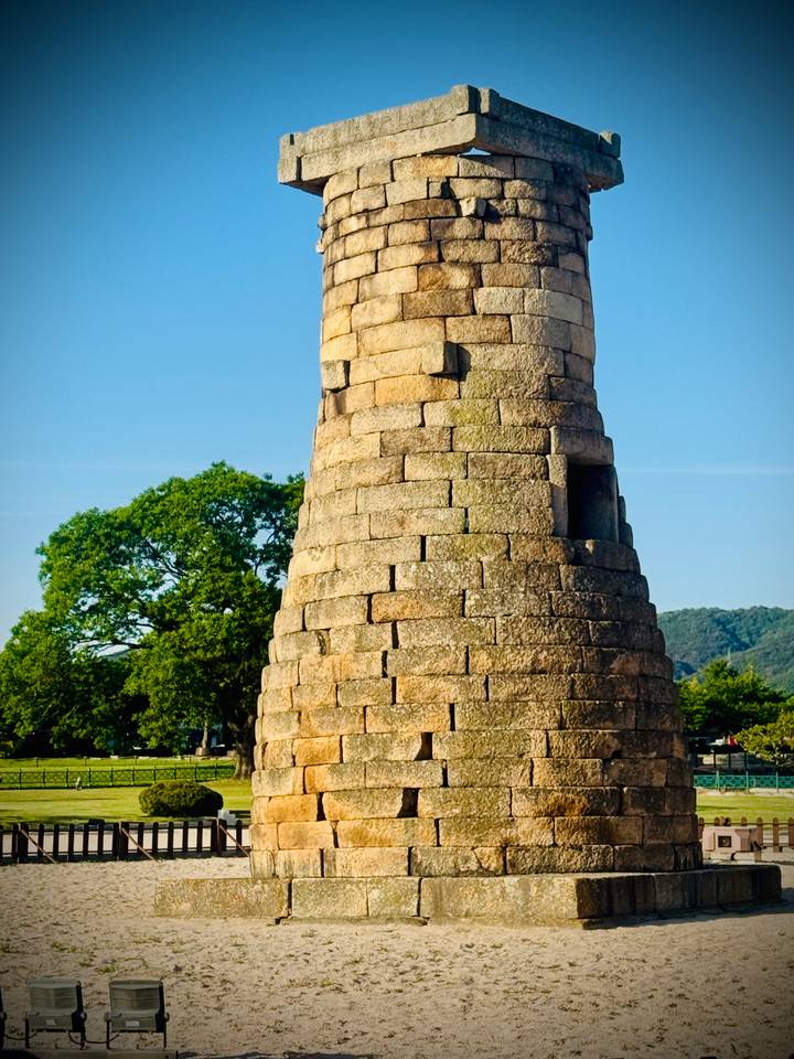 Stone Cheomseongdae Observatory tower standing beside leafy tree under clear sky